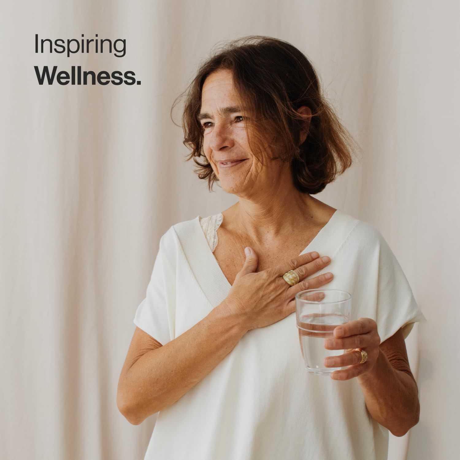 Femme tenant un verre d'eau. Inspiring Wellness. La femme sourit. Elle porte une bague.