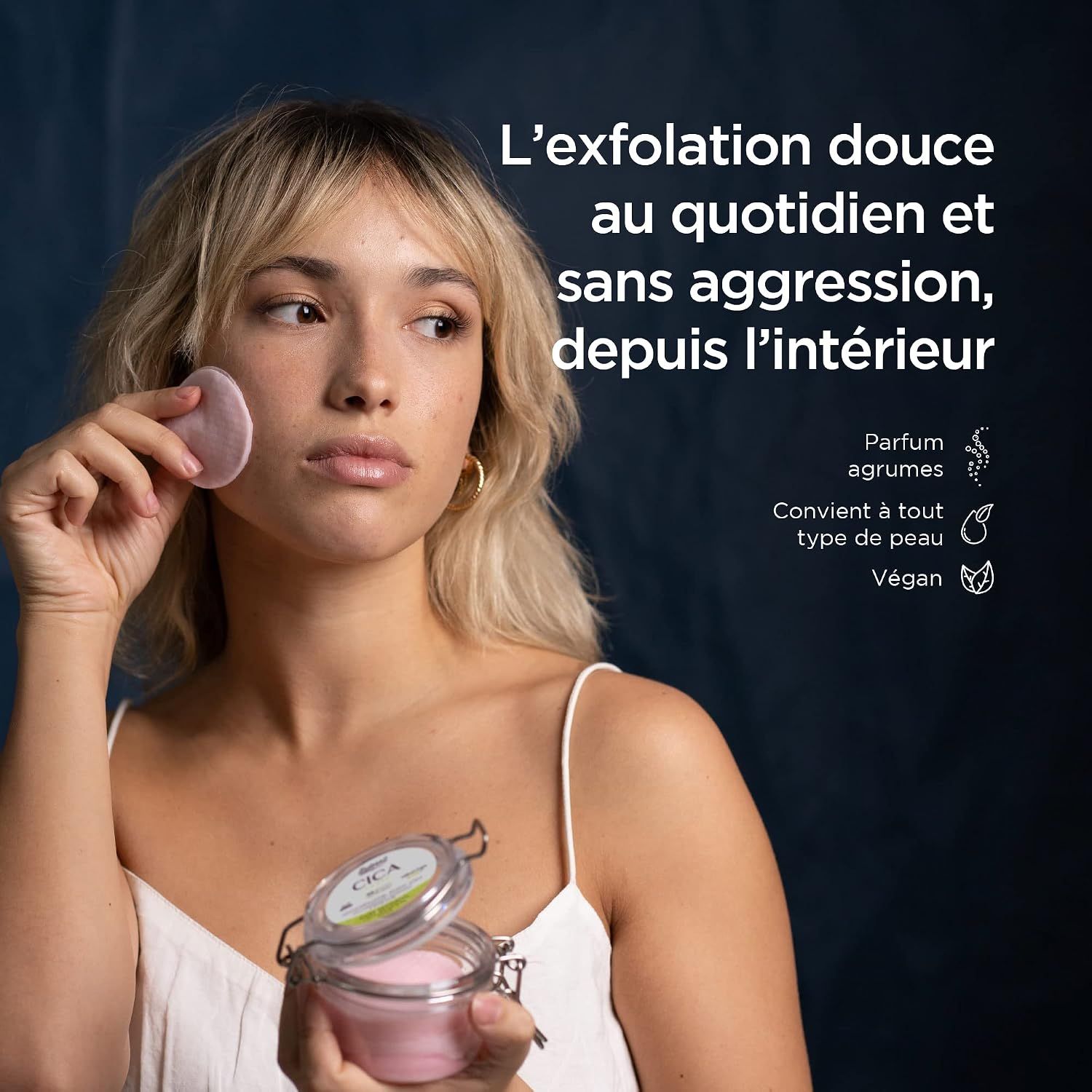 Femme tenant des cotons roses dans un bocal et un coton sur sa joue. "CICA" et "Vegan" sont visibles sur l'étiquette.