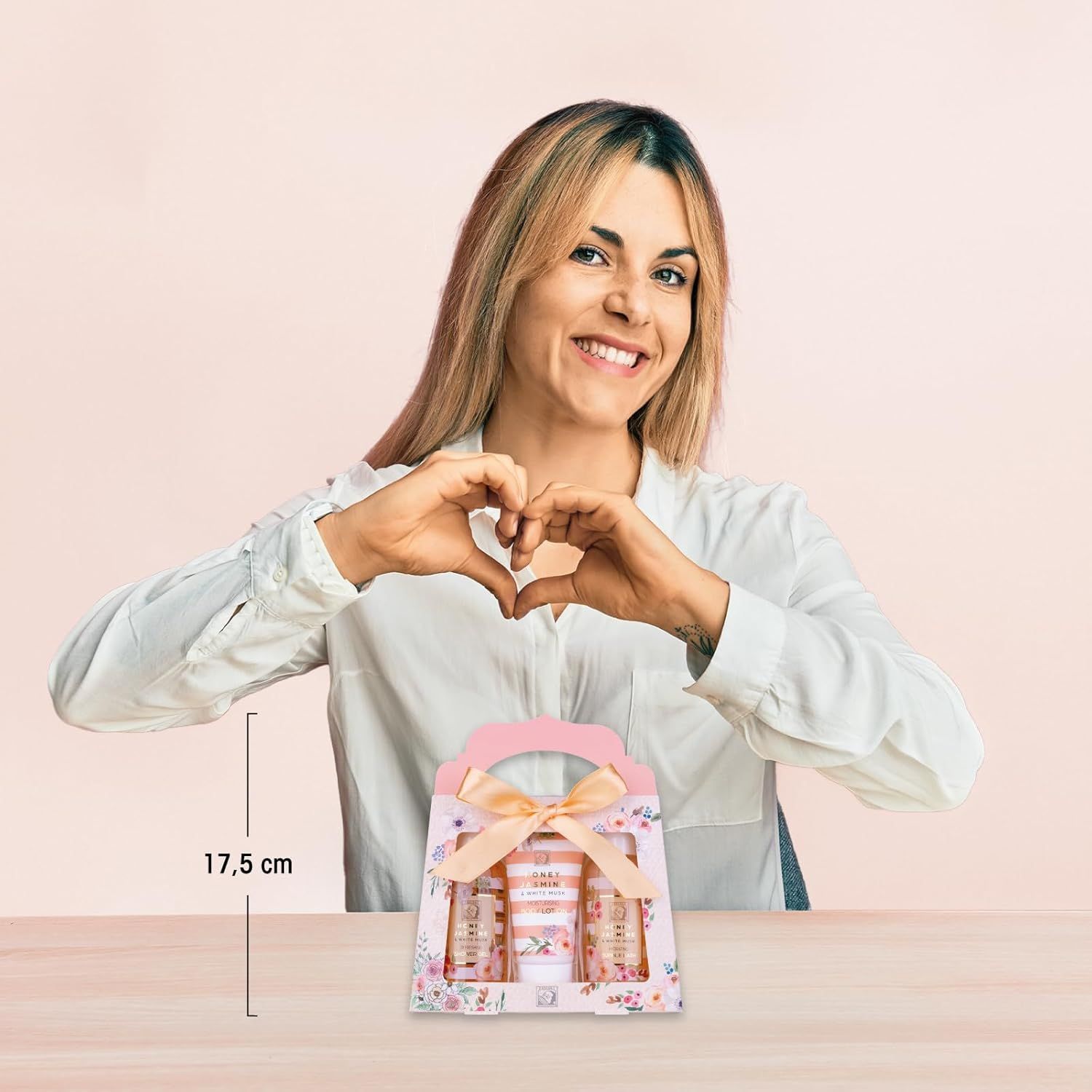 Vrouw vormt hart met handen. Cadeaudoos met drie producten: douchegel, badschuim, bodylotion. Doos met strik en bloemmotief.