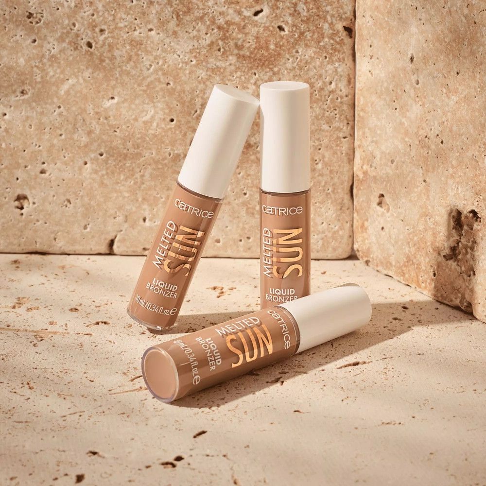 Trois flacons de bronzer liquide. Inscription: Melted Sun, Liquid Bronzer, Catrice. Placé sur une dalle de pierre.