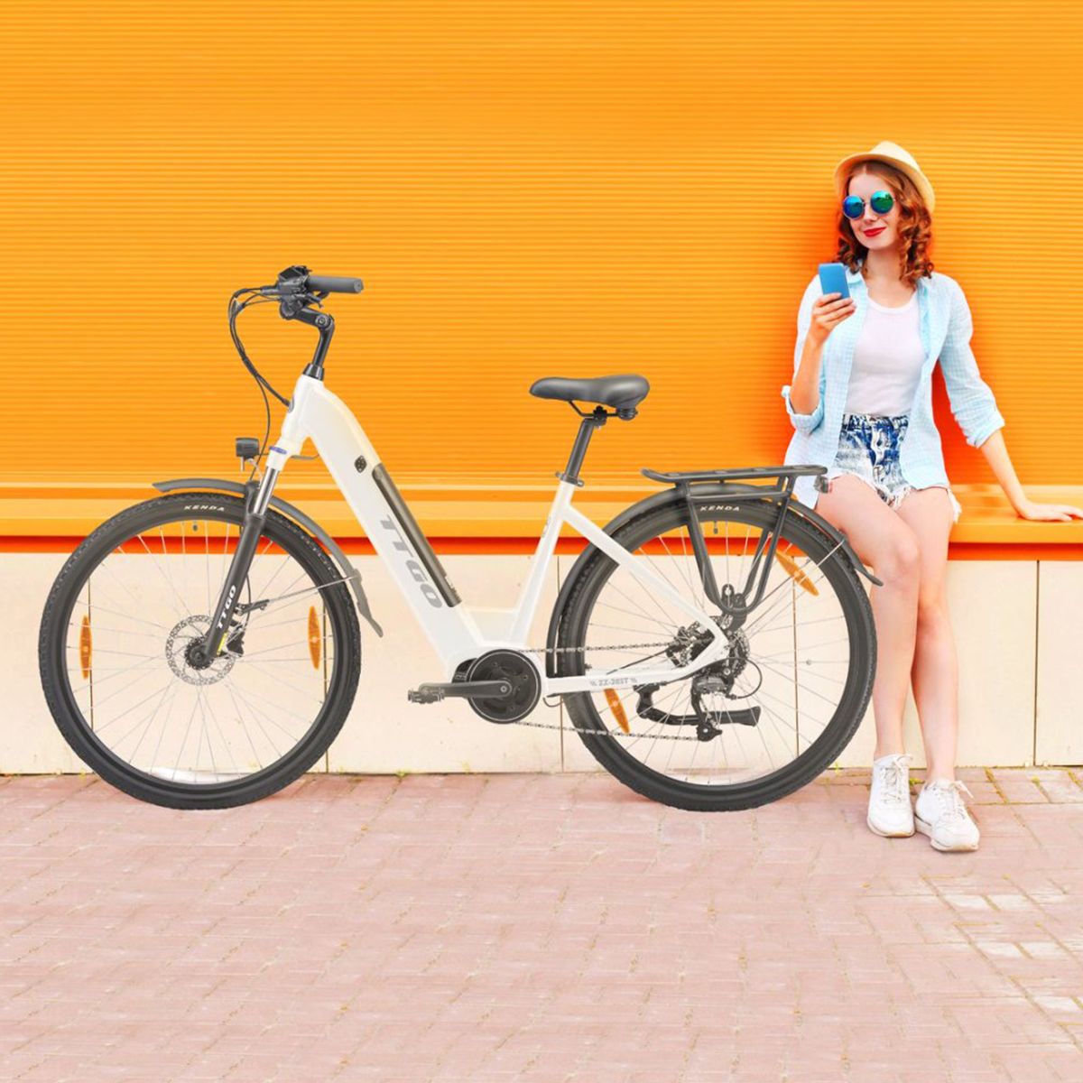 Une femme assise à côté d'un vélo électrique blanc. Le vélo a des pneus noirs et un porte-bagages.