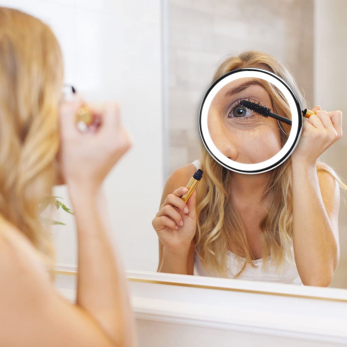 Femme utilisant un miroir grossissant éclairé pour le maquillage.
