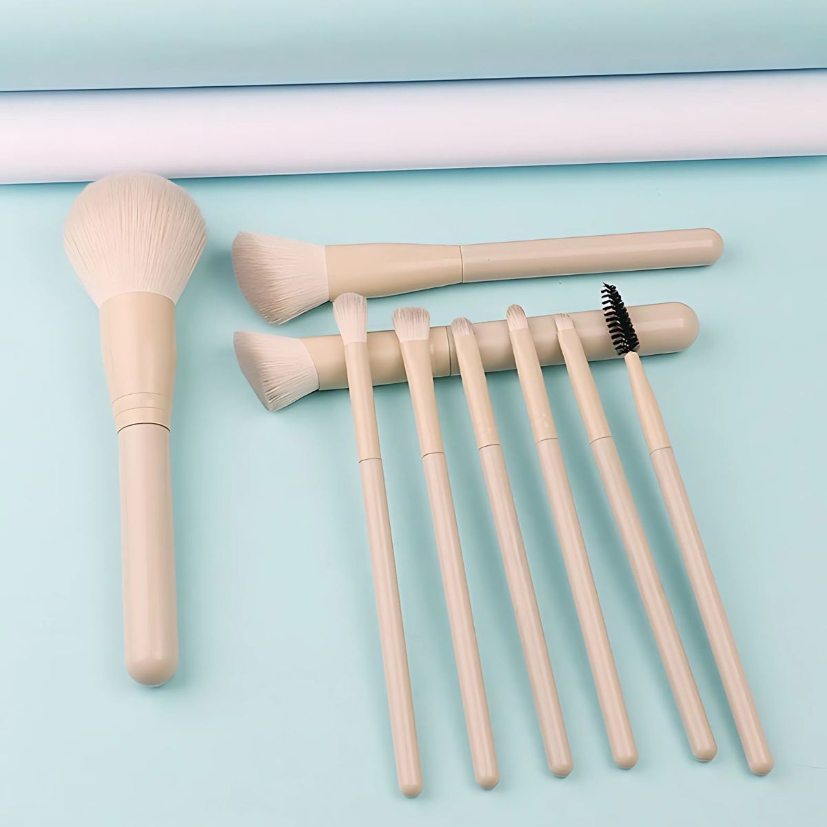 Un ensemble de huit pinceaux de maquillage beige clair avec différentes têtes, dont un grand pinceau poudre et des plus petits pour les yeux et les lèvres.