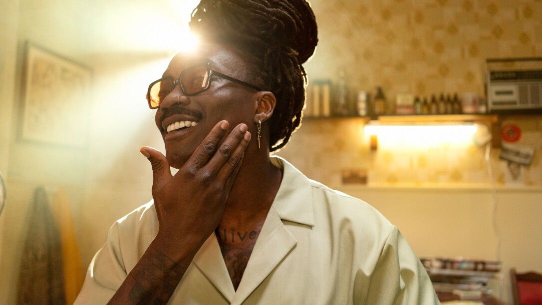 Un homme se touche le visage. Il porte des lunettes et une chemise claire. La lumière du soleil brille.