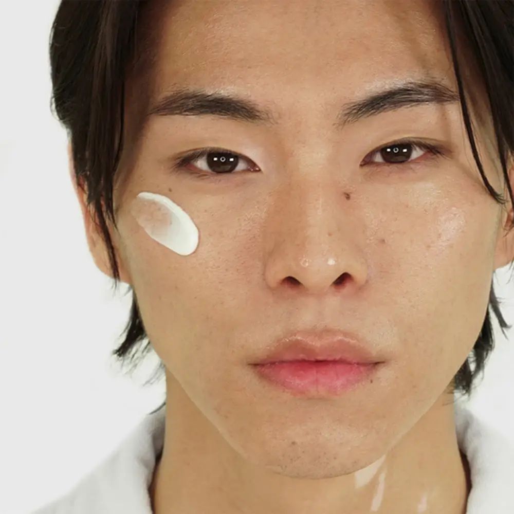 Gros plan d'un homme. Une crème blanche est appliquée sur la joue.