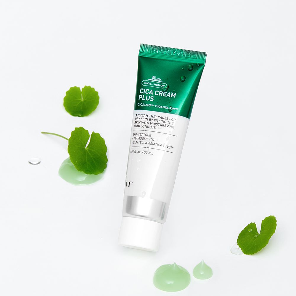 Tube de Cica Cream Plus. Tube vert et blanc avec nom et ingrédients. Feuilles et gouttes de crème verte à côté.