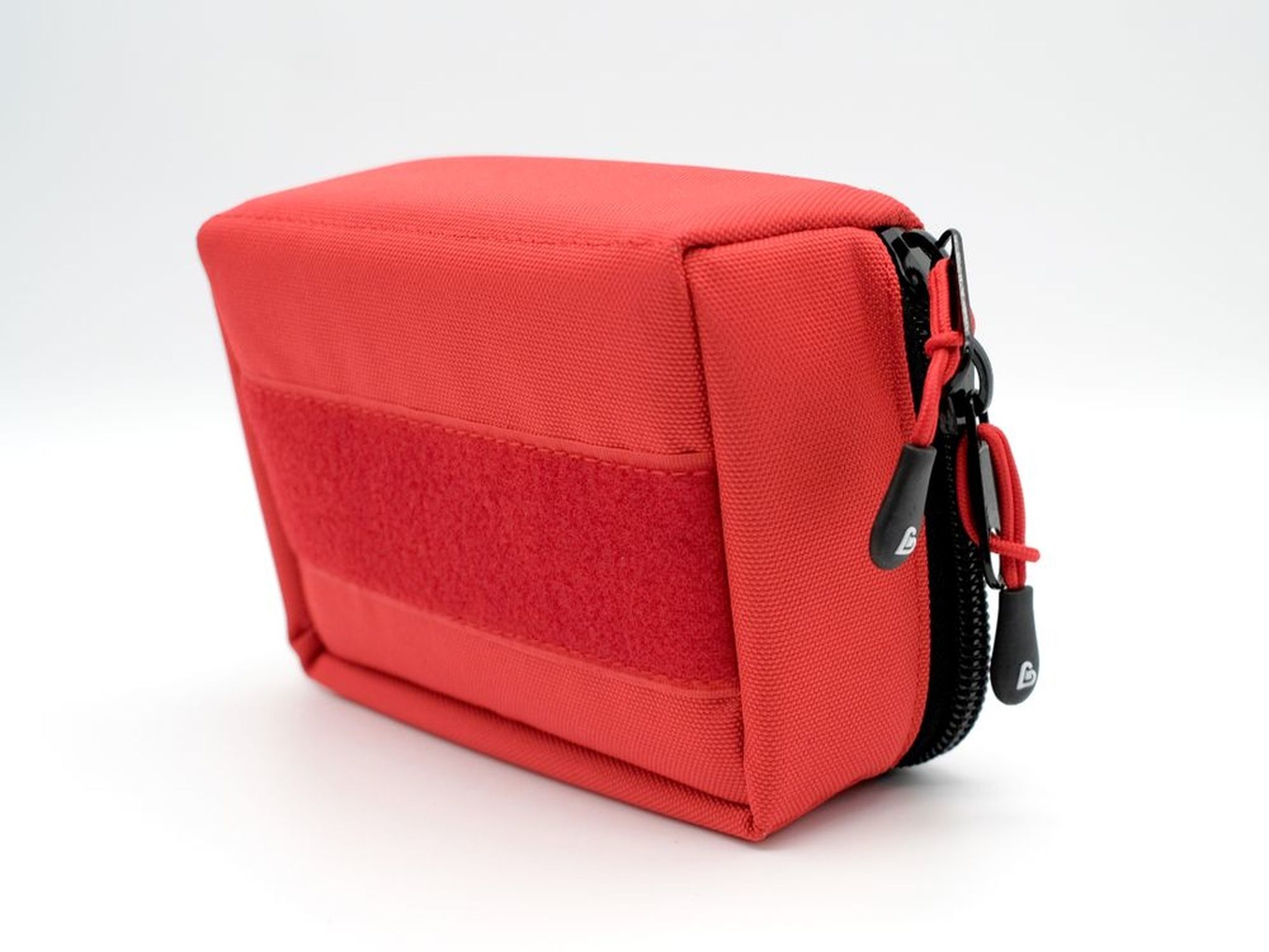 Pochette d'urgence rouge avec surface velcro sur le côté et tirettes de fermeture éclair noires.