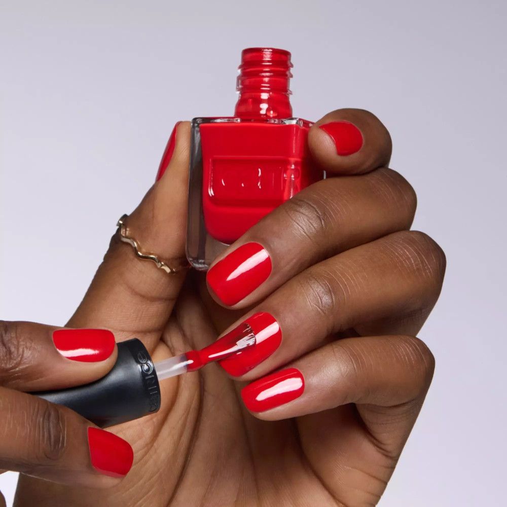 Main avec ongles rouges vernis et vernis à ongles. Application au pinceau. Marque Catrice.