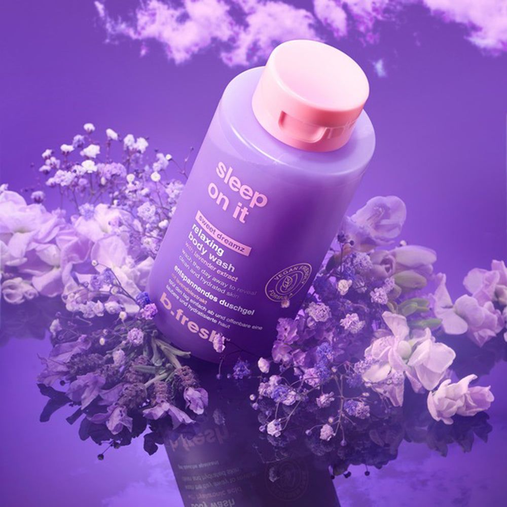 Bouteille violette de gel douche relaxant "sleep on it", entourée de fleurs violettes et blanches.