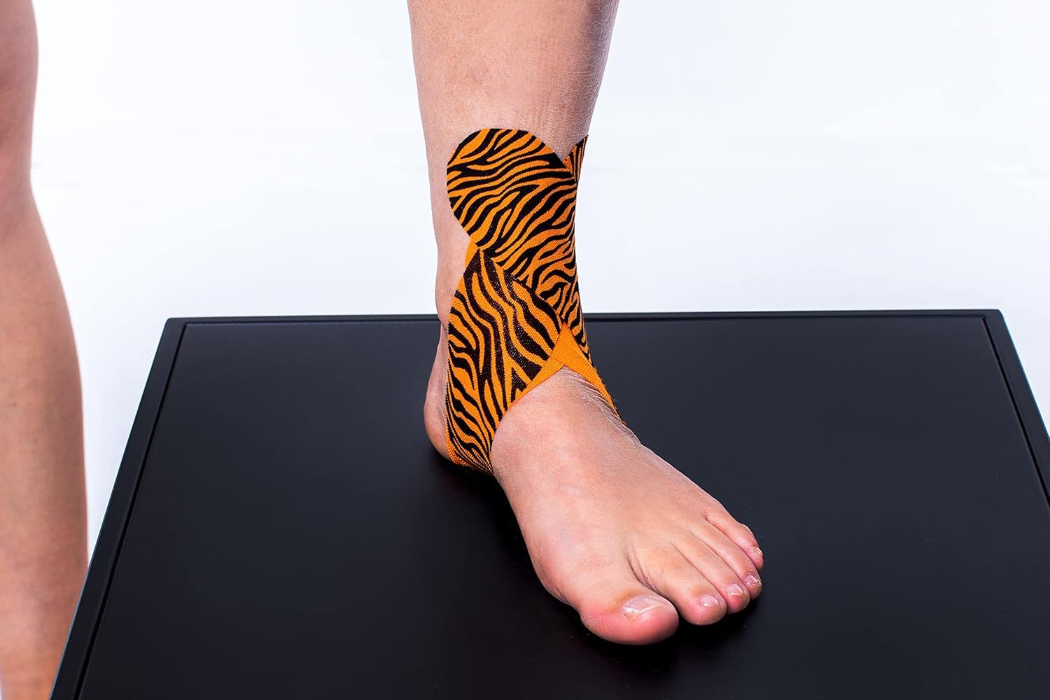 CureTape kinesiologie tape met tijgerprint, aangebracht op de enkel van een voet. Toont de tape-applicatie.
