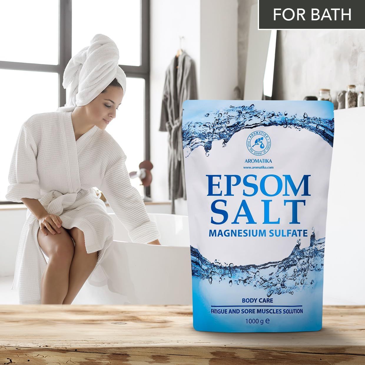 Femme en peignoir et serviette à côté d'une baignoire et d'un sachet de sel d'Epsom AROMATIKA.