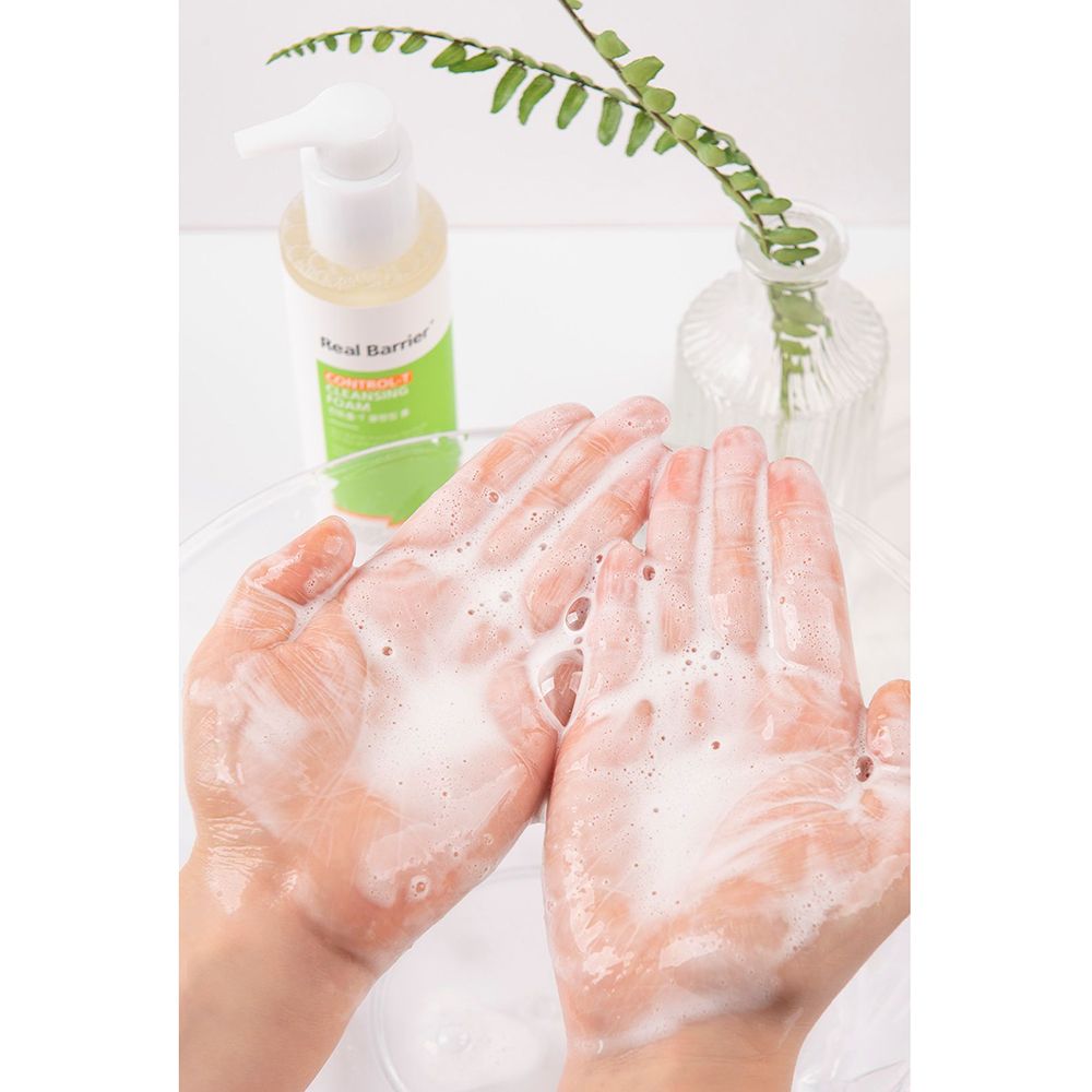 Handen met schuim. Fles met pomp op de achtergrond. Tekst: Real Barrier, Control-T Cleansing Foam. Kom met vloeistof.