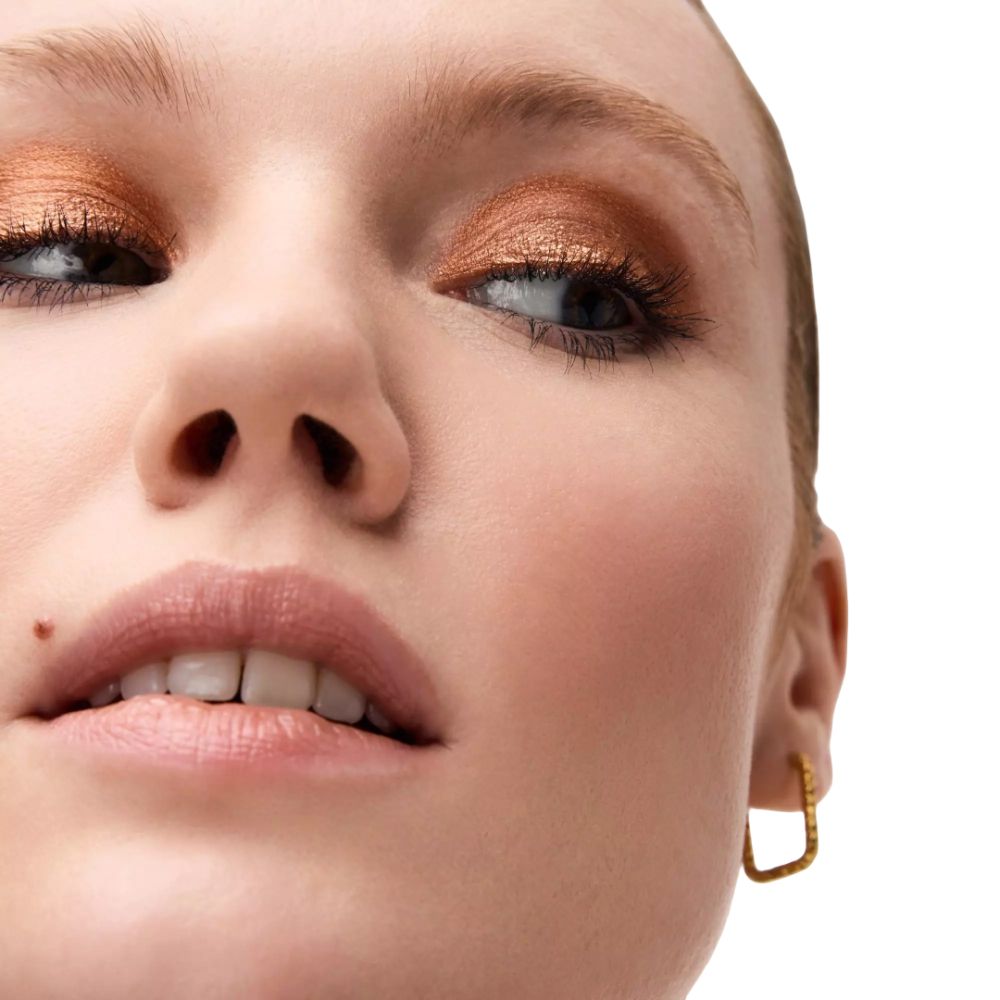 Close-up van een gezicht met gouden oogschaduw. De persoon draagt gouden oorbellen. Witte achtergrond.