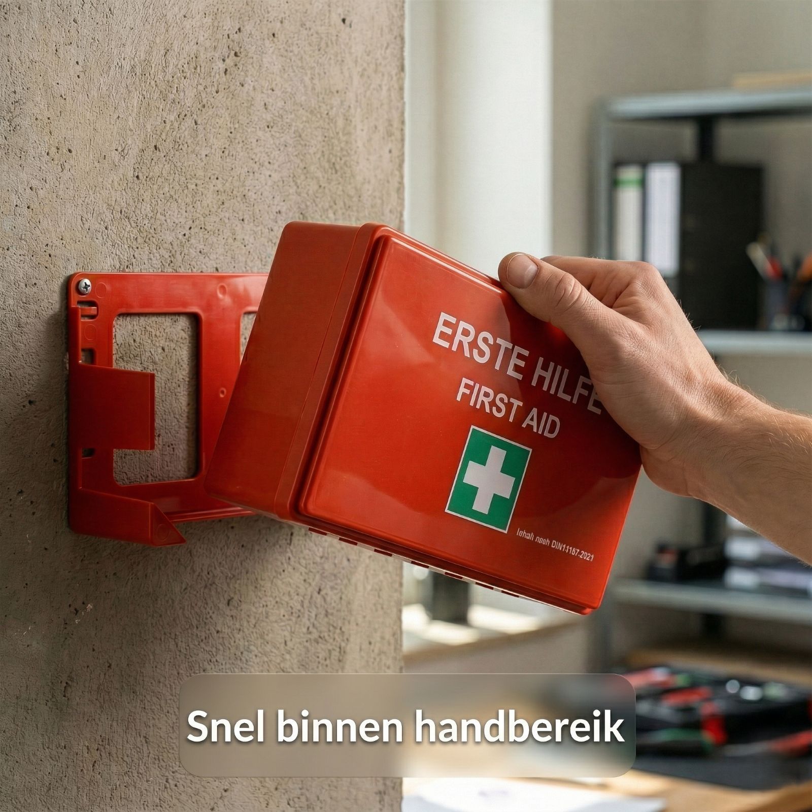 Rode EHBO-koffer aan muurbeugel. Opschrift: Erste Hilfe/First Aid. Groen kruis. Snel binnen handbereik.