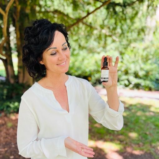 Vrouw houdt productfles vast. Fles met tekst: CERTIFIED ORGANIC ILLUMINATING SERUM. Vrouw lacht.