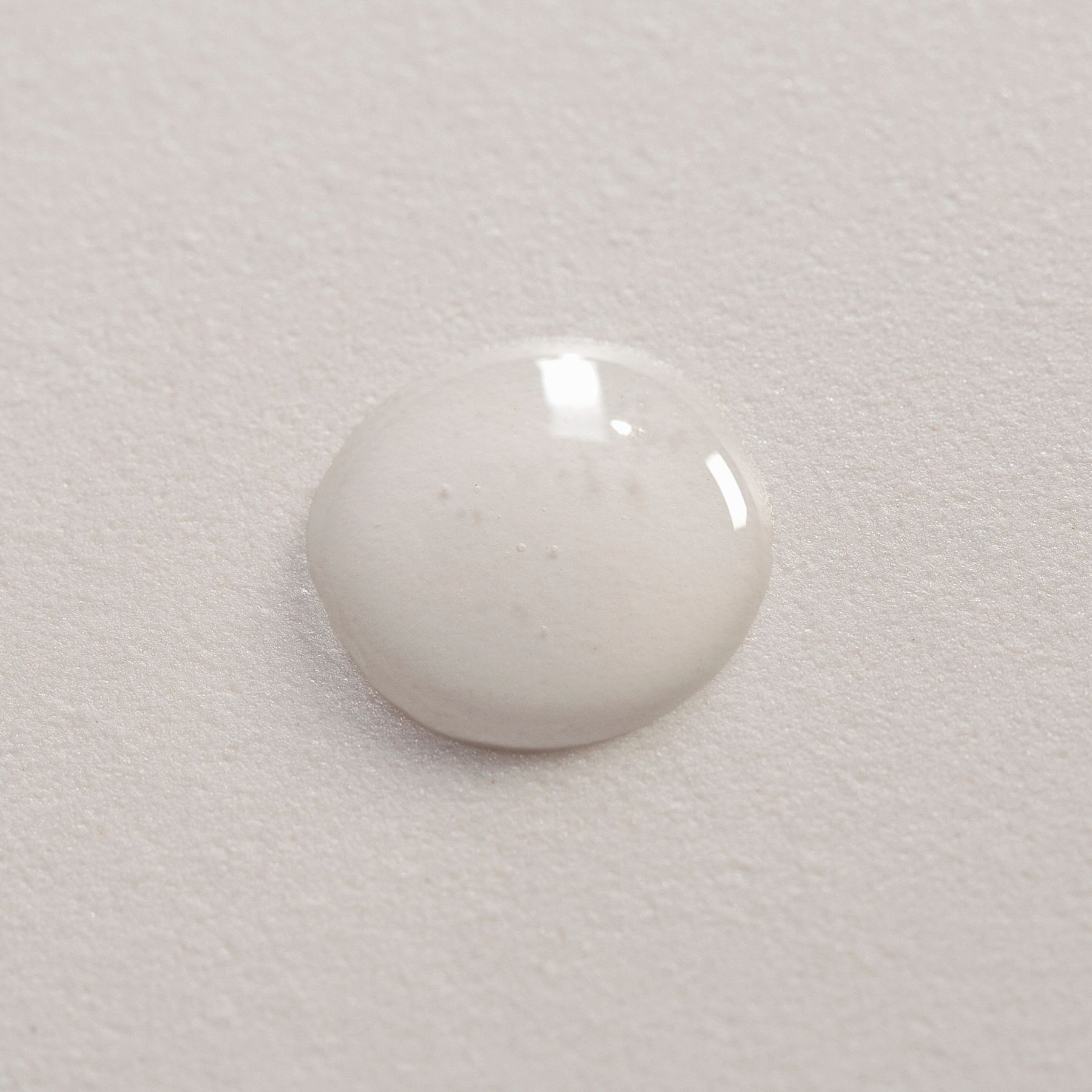 Een druppel wit serum op een getextureerd oppervlak.