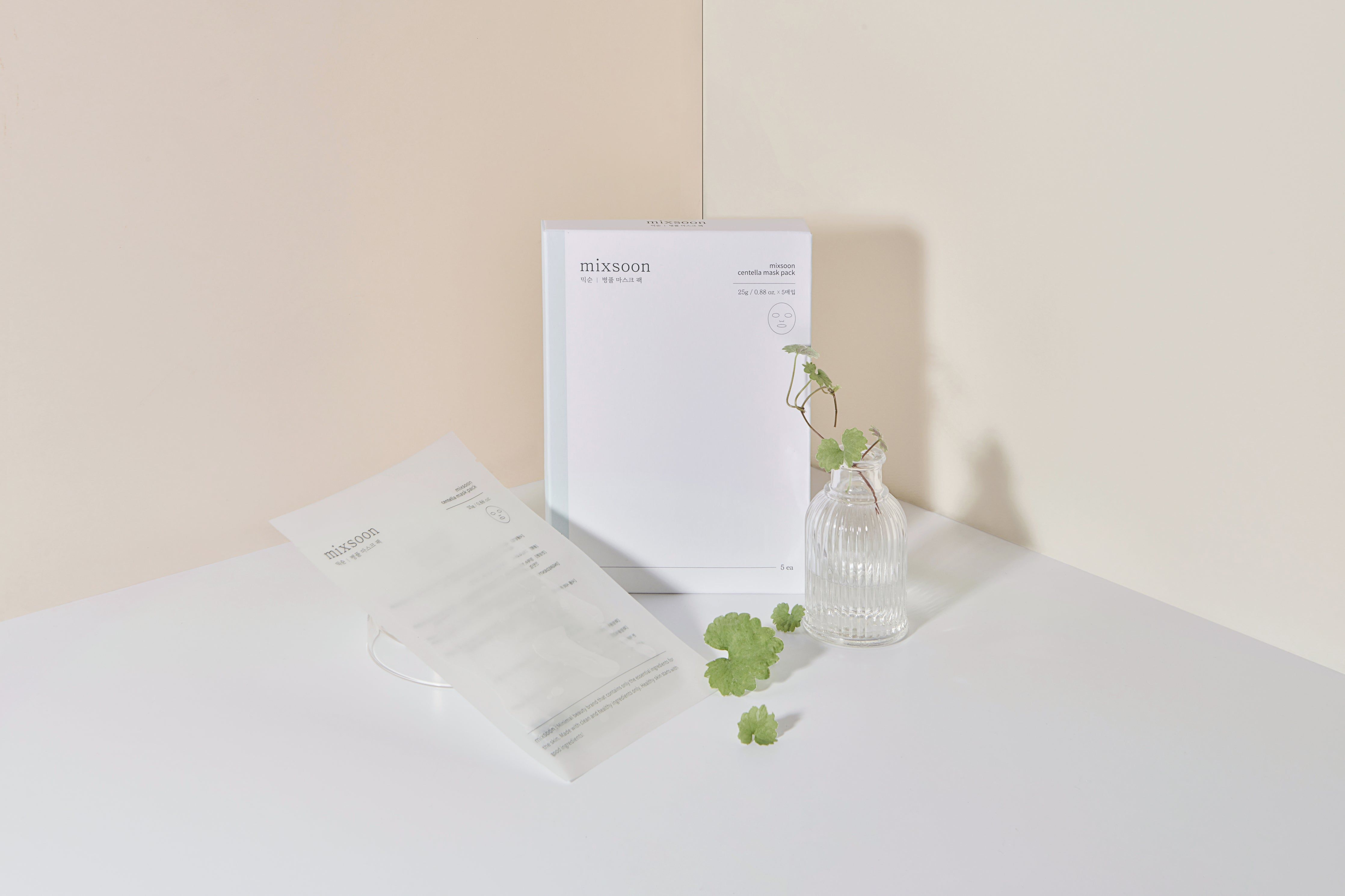Emballage Mixsoon Centella Mask Pack. Paquet blanc rectangulaire. À côté, vase transparent avec feuilles vertes.