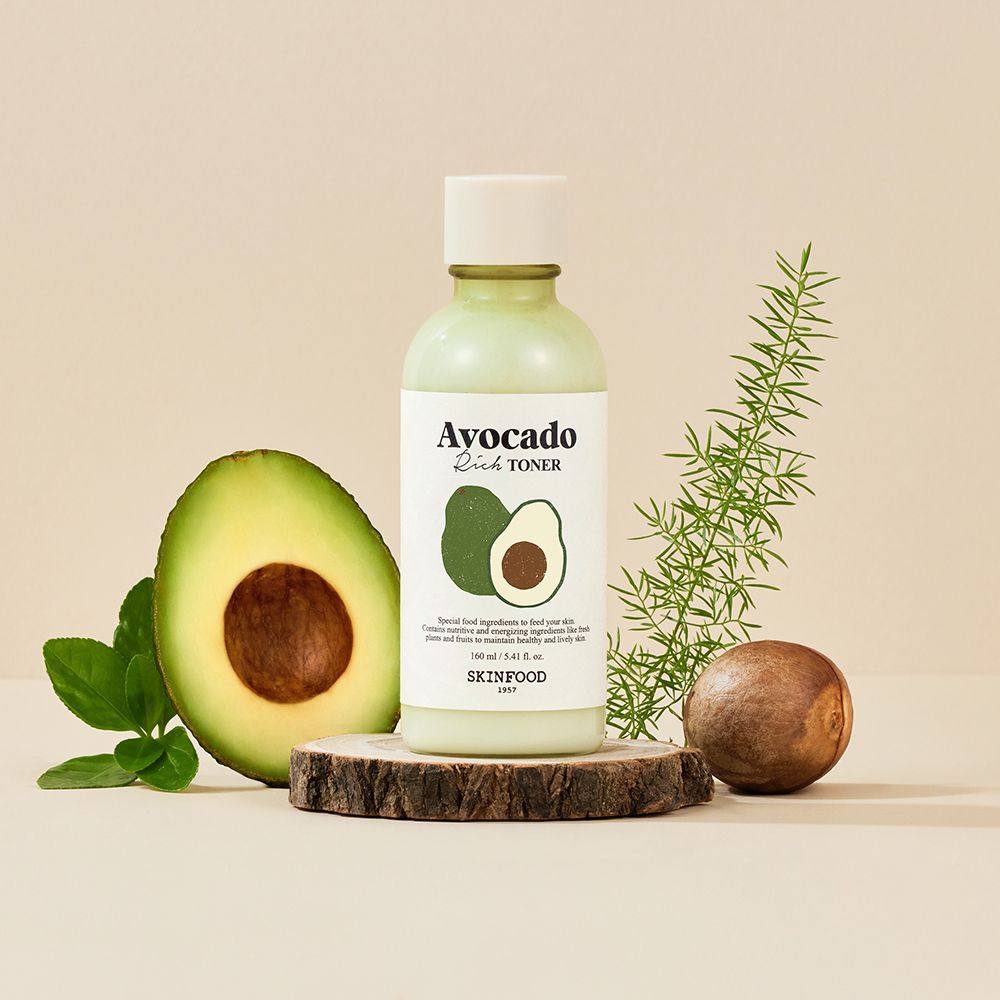 Flacon vert Avocado Rich Toner, SKINFOOD. Demi-avocat, branche et rondin de bois. Texte Avocado Rich Toner.