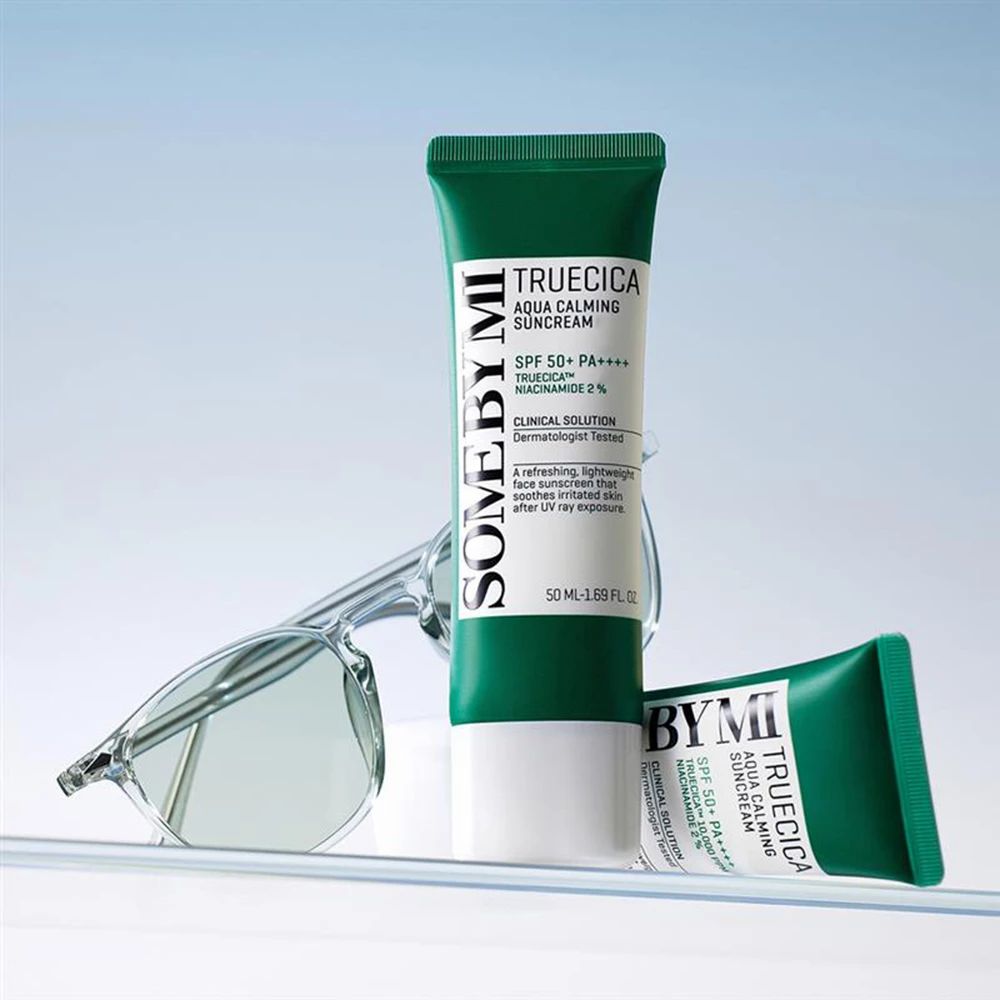 Deux tubes de crème solaire, bouchon vert, corps blanc. Texte : SOMEBYMI, TRUECICA Aqua Calming Suncream, SPF 50+ PA++++. Lunettes.
