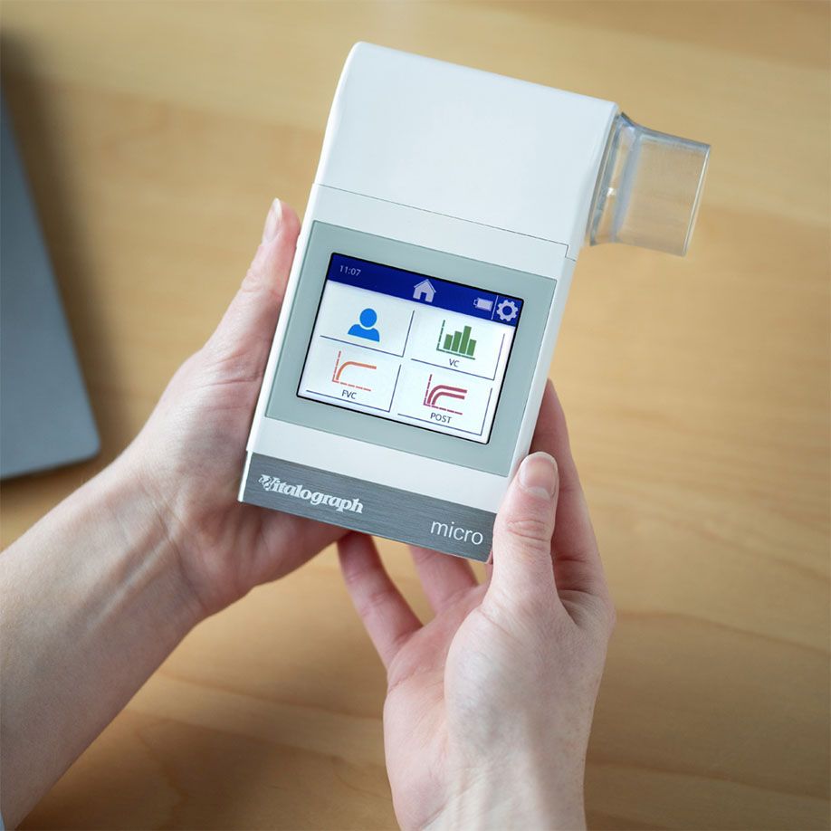 Persoon houdt Vitalograph micro hand-spirometer vast met touchscreen display dat longfunctie-grafieken toont.