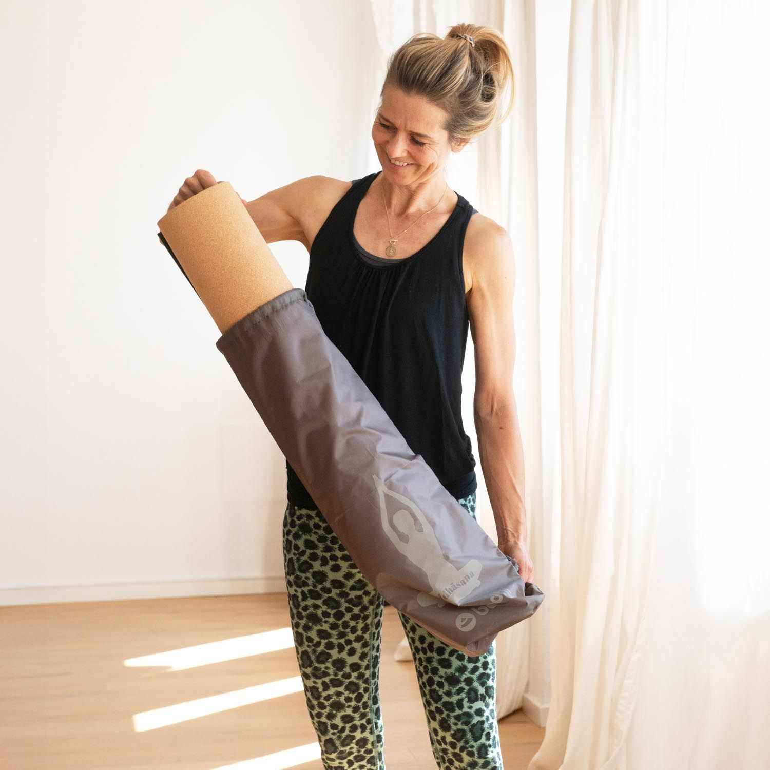 Vrouw houdt een grijze yogamat tas vast, waar een yogamat uit steekt.