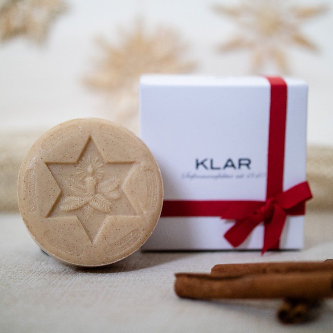 Ronde zeep met sterpatroon en opschrift. Witte geschenkdoos met rode strik. Kaneelstokjes.