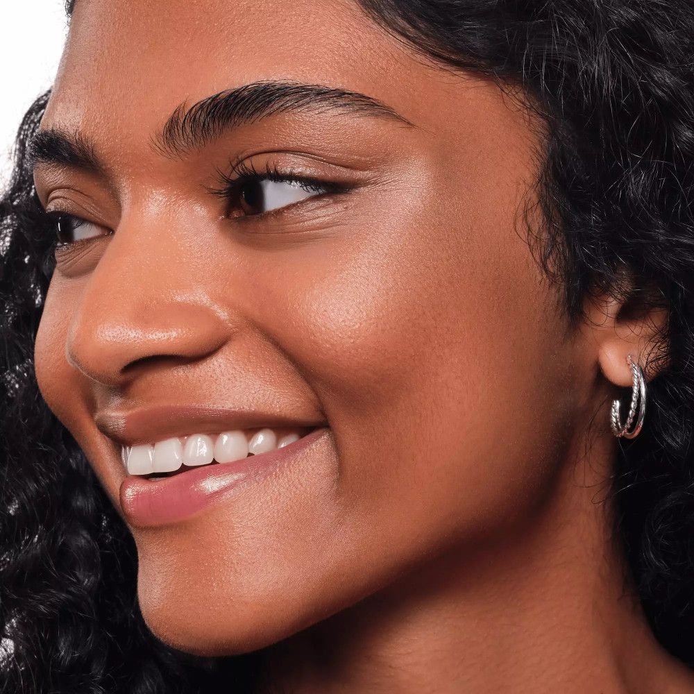 Close-up van een lachende vrouw. Huid geaccentueerd met highlighter. Zilveren oorringen.