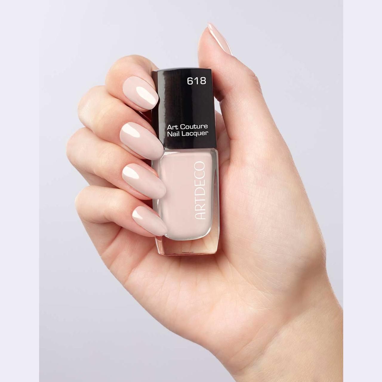 Hand houdt nagellakfles en gelakte nagels vast. Lichtroze nagellak. Opschrift 618. Art Couture Nail Lacquer.