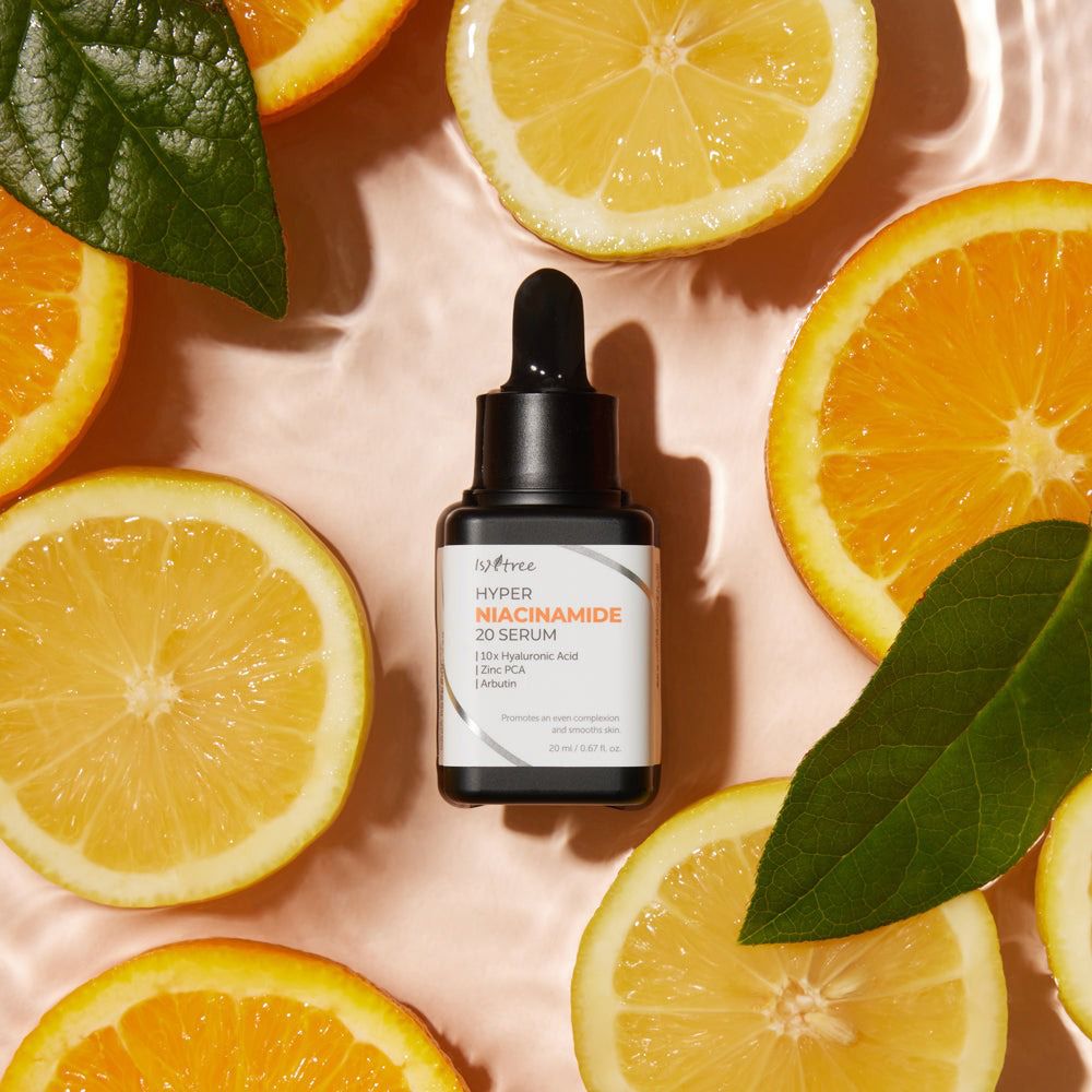 Flacon de sérum avec compte-gouttes, entouré de tranches de citrons et d'oranges. Inscription : ISNTREE Hyper Niacinamide 20 Serum. Flacon noir.