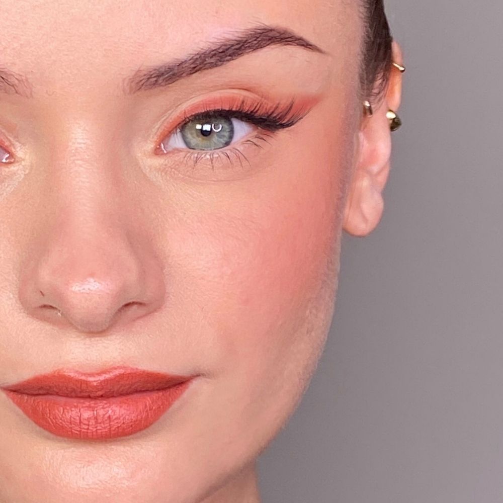 Close-up van een gezicht met opgemaakte ogen, wangen en lippen. Koraalrode lippenstift. Lichte huidskleur.