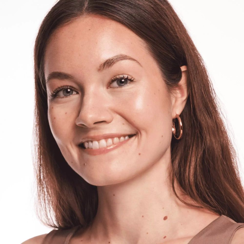 Portret van een lachende vrouw met bruin haar. Ze draagt gouden oorringen. Natuurlijke make-up.