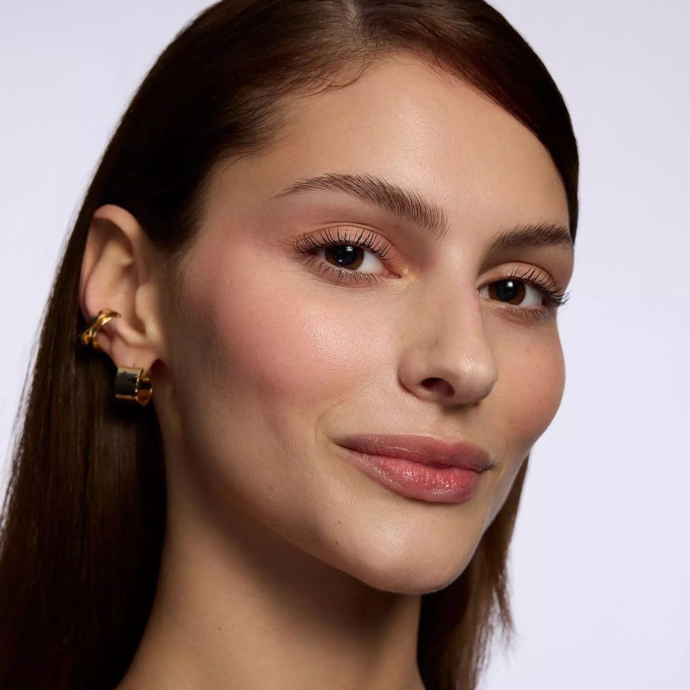 Portrait d'une femme aux cheveux châtain clair et aux boucles d'oreilles dorées. Lèvres légèrement maquillées.