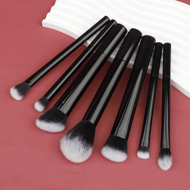 Sept pinceaux de maquillage noirs avec poils blancs, sur fond blanc. Différentes formes.