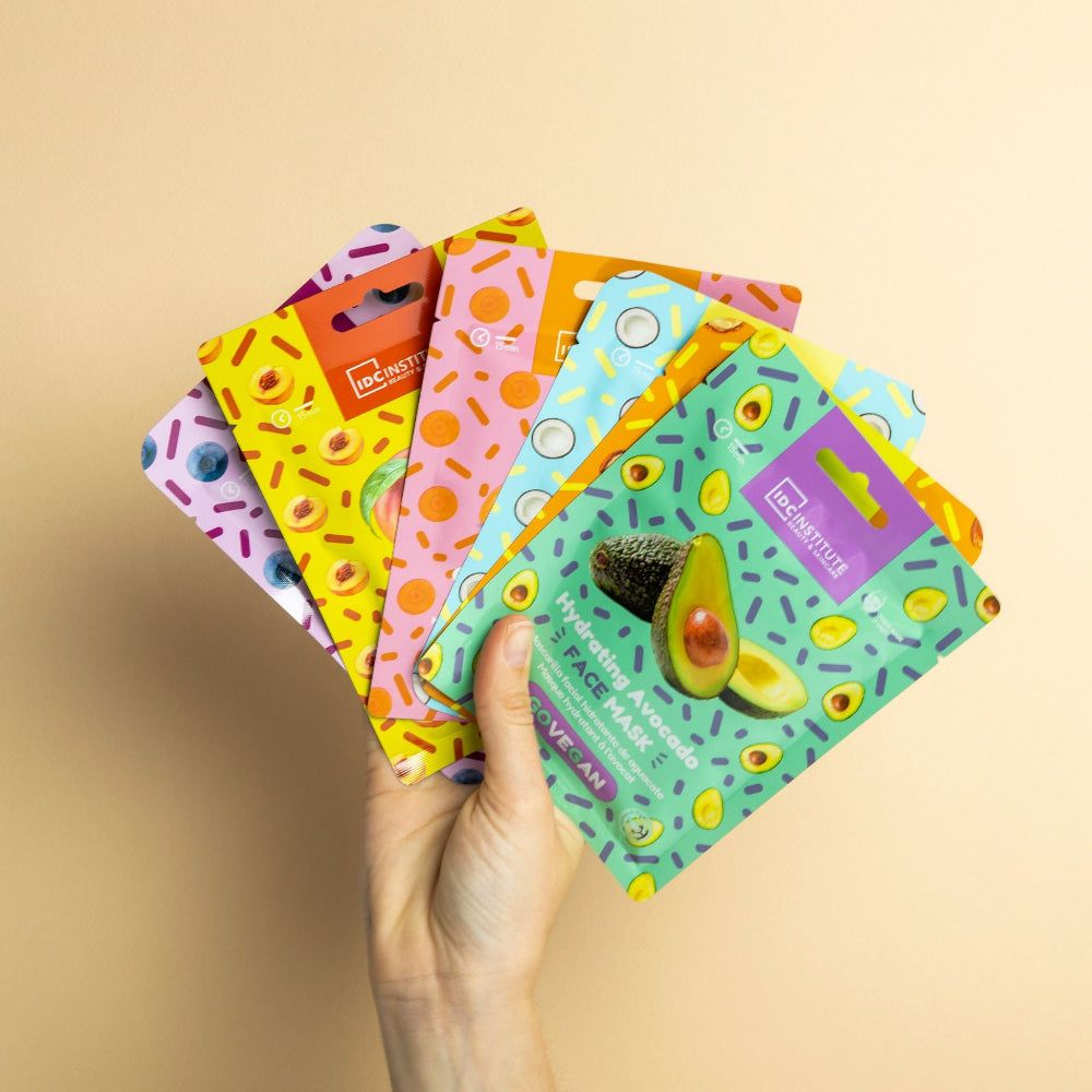 Main tenant plusieurs masques faciaux colorés. Différents designs avec avocat, noix de coco et autres fruits.