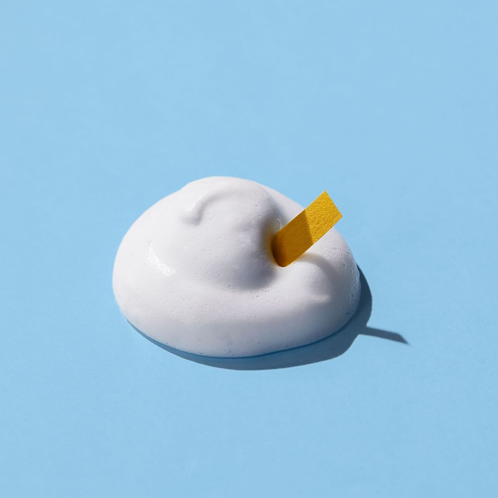 Hoop witte schuim op blauwe achtergrond. Gele strook steekt in het schuim.