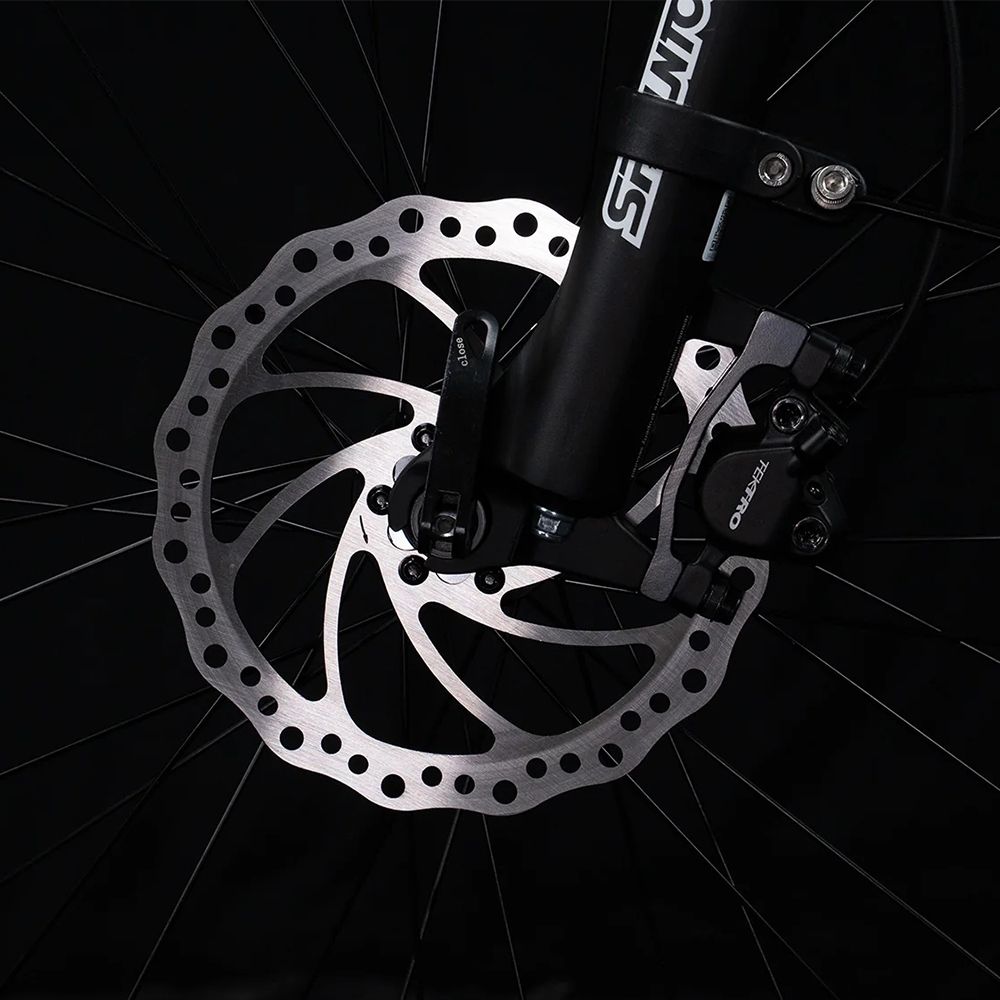 Gros plan sur le frein à disque d'un vélo. Disque de frein argenté avec étrier noir.