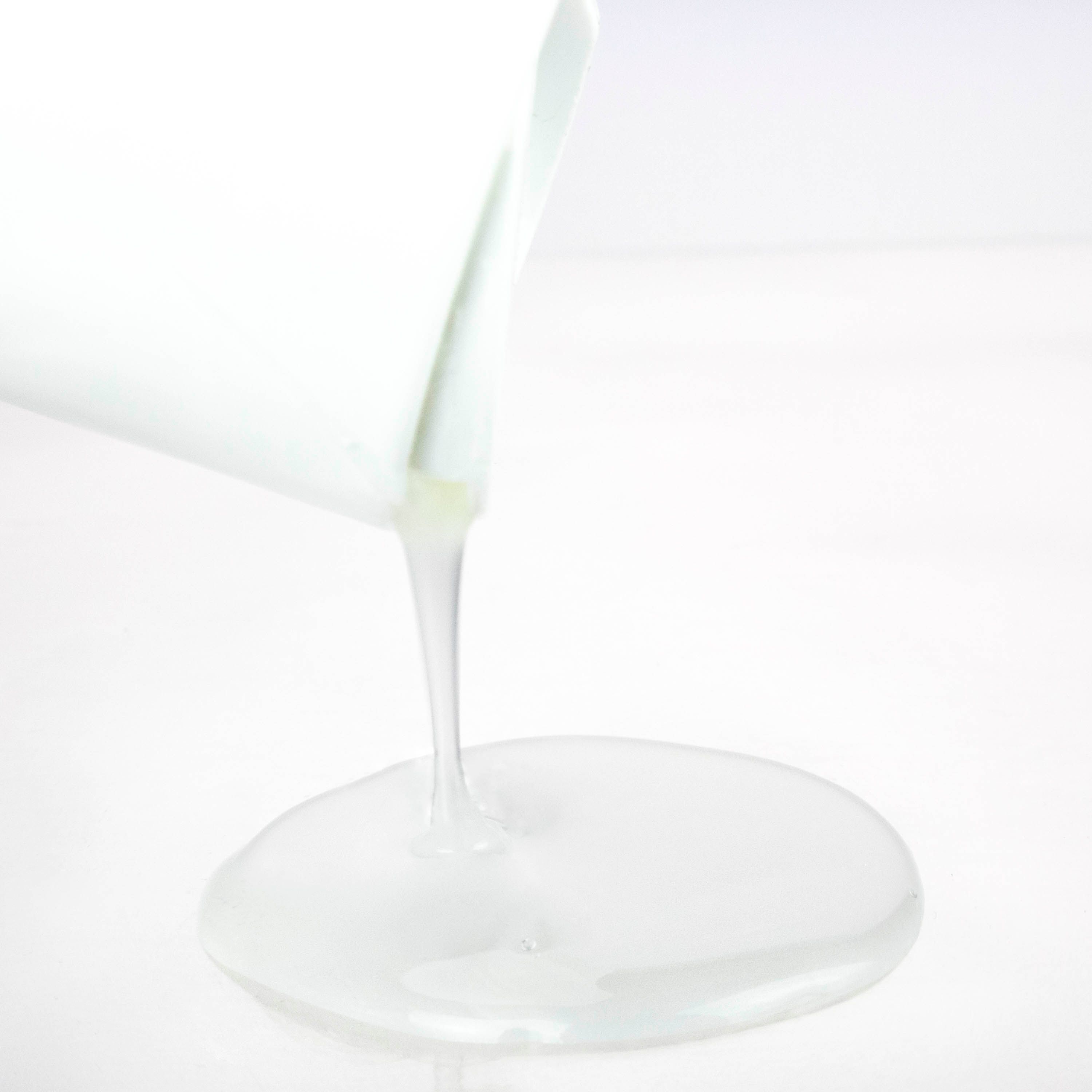 Liquide s'écoulant d'un flacon blanc. Le liquide est blanc et forme une flaque plate sur une surface blanche.