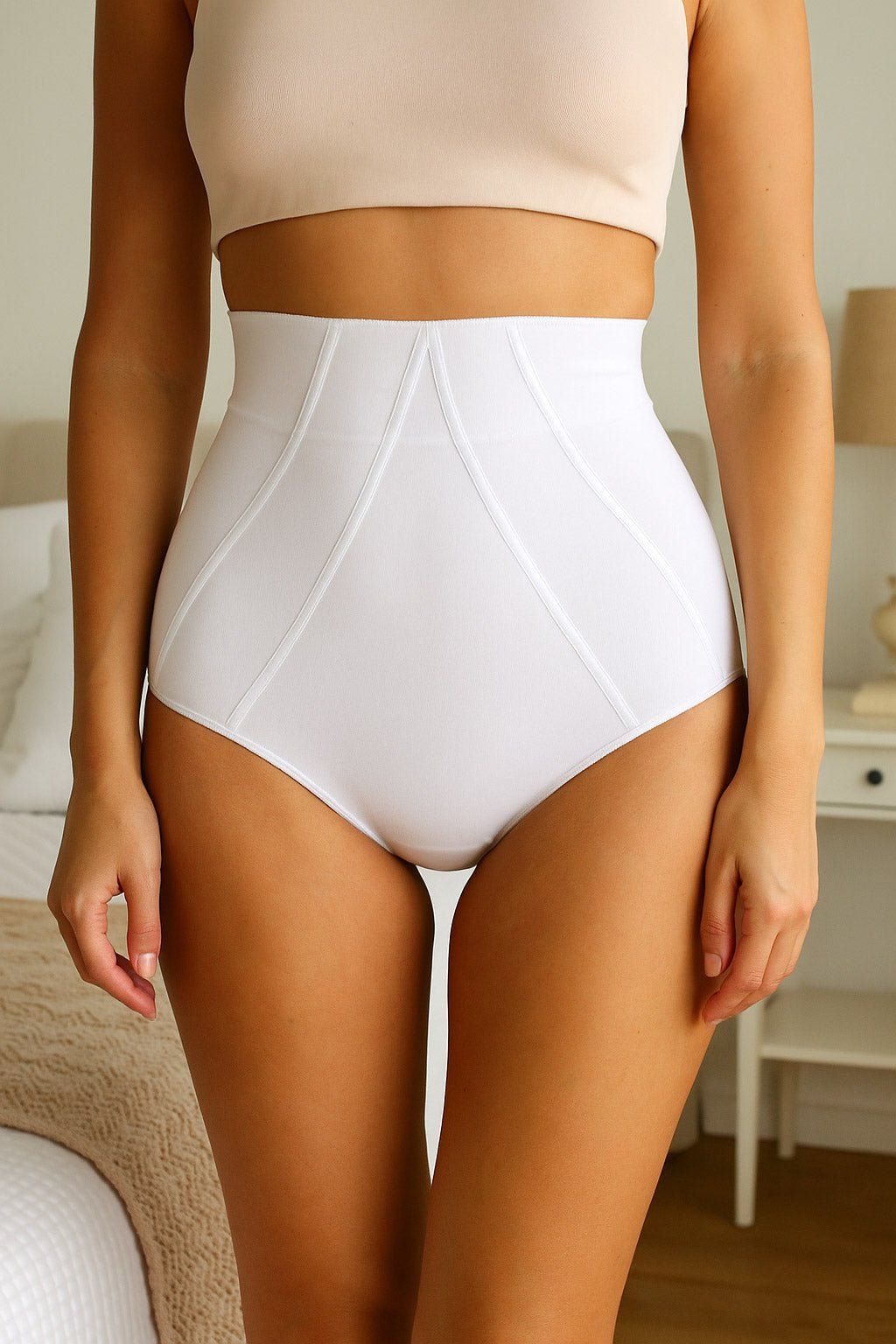 Witte corrigerende slip met hoge taille. Katoen. Naden. Vrouw draagt het product. Bed en nachtkastje op de achtergrond.