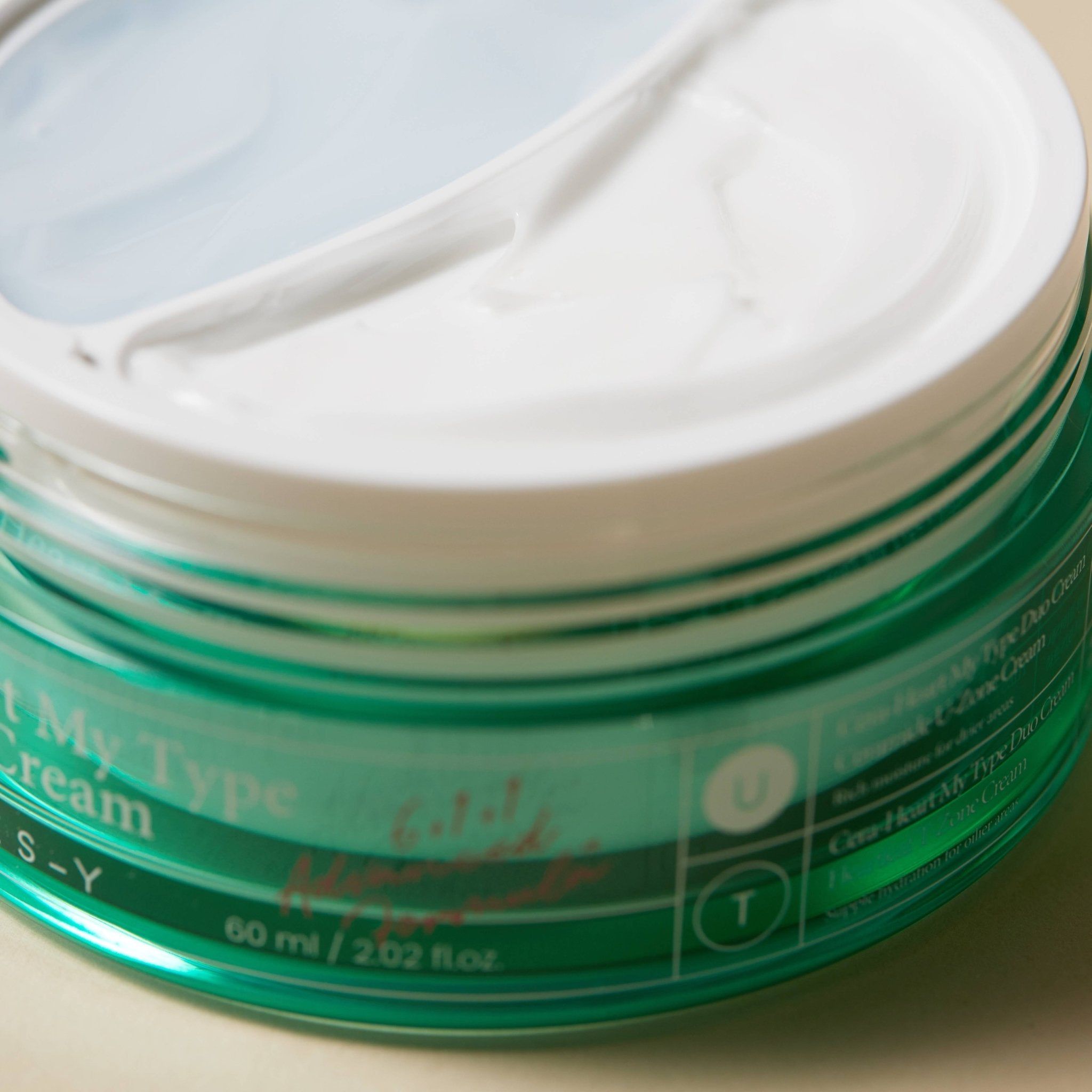 Close-up van een groene crème pot met witte deksel. Opschrift: Cera-Heart My Type Duo Cream.