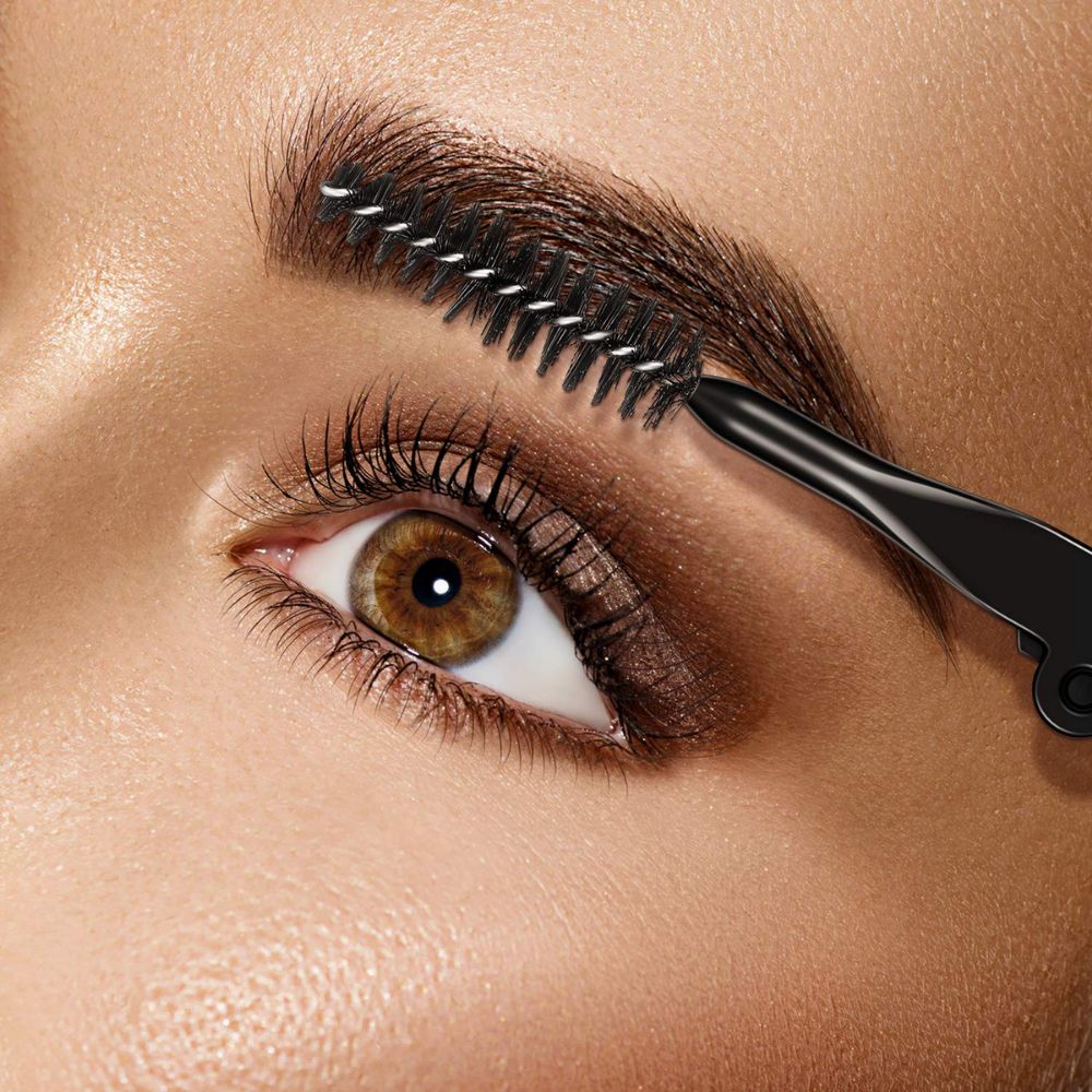 Gros plan d'une brosse à sourcils coiffant un sourcil. Manche noir, poils fins.
