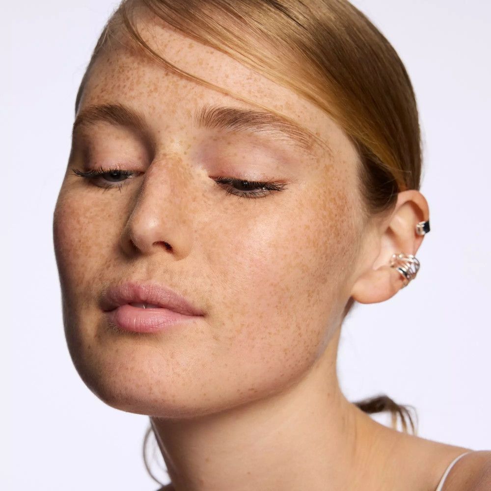 Portrait d'une femme avec des taches de rousseur. Yeux fermés, bouche légèrement ouverte. Boucle d'oreille à l'oreille.