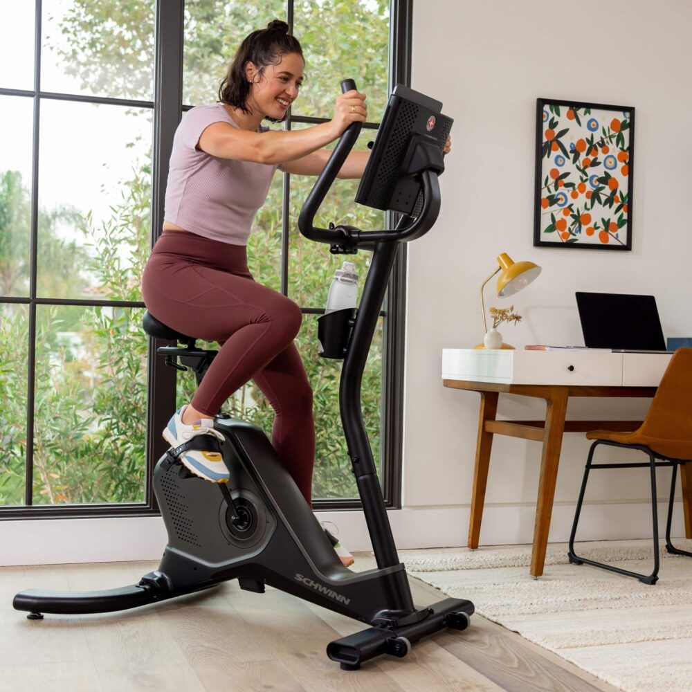 Femme faisant de l'exercice sur un Schwinn 590U noir. Bouteille d'eau sur le guidon. Bureau en arrière-plan.
