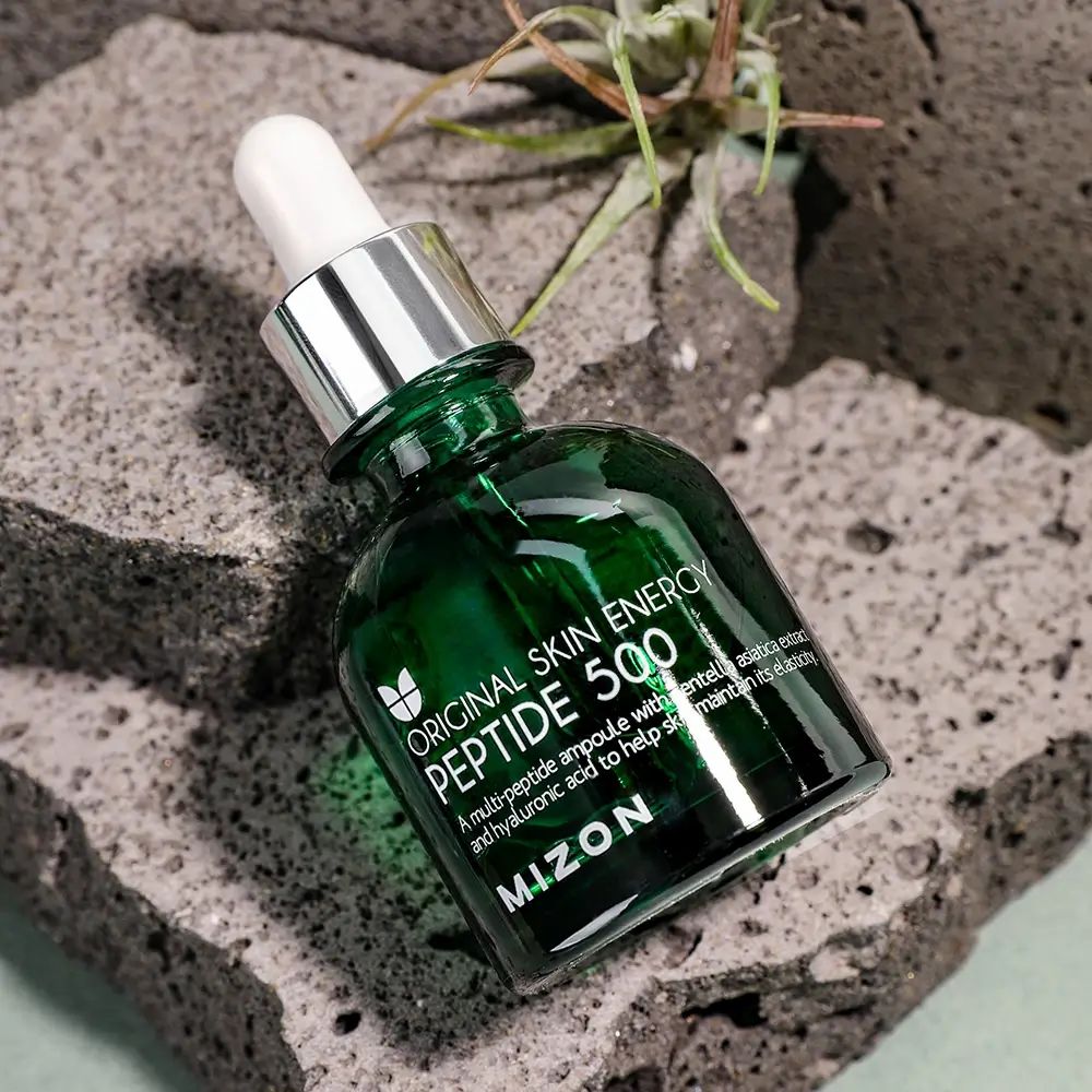 Groene glazen fles met pipet op steen. Opschrift: ORIGINAL SKIN ENERGY PEPTIDE 500, MIZON.