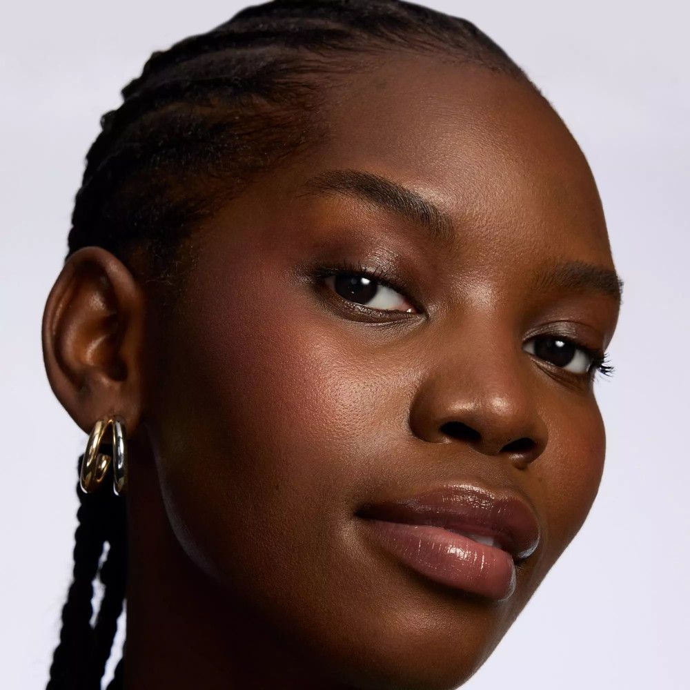 Portrait d'une femme à la peau foncée, aux cheveux tressés et aux boucles d'oreilles dorées. Lèvres légèrement maquillées.
