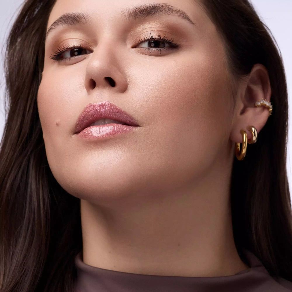 Close-up van een vrouw met glanzende lipgloss op haar lippen. Ze draagt gouden oorbellen.