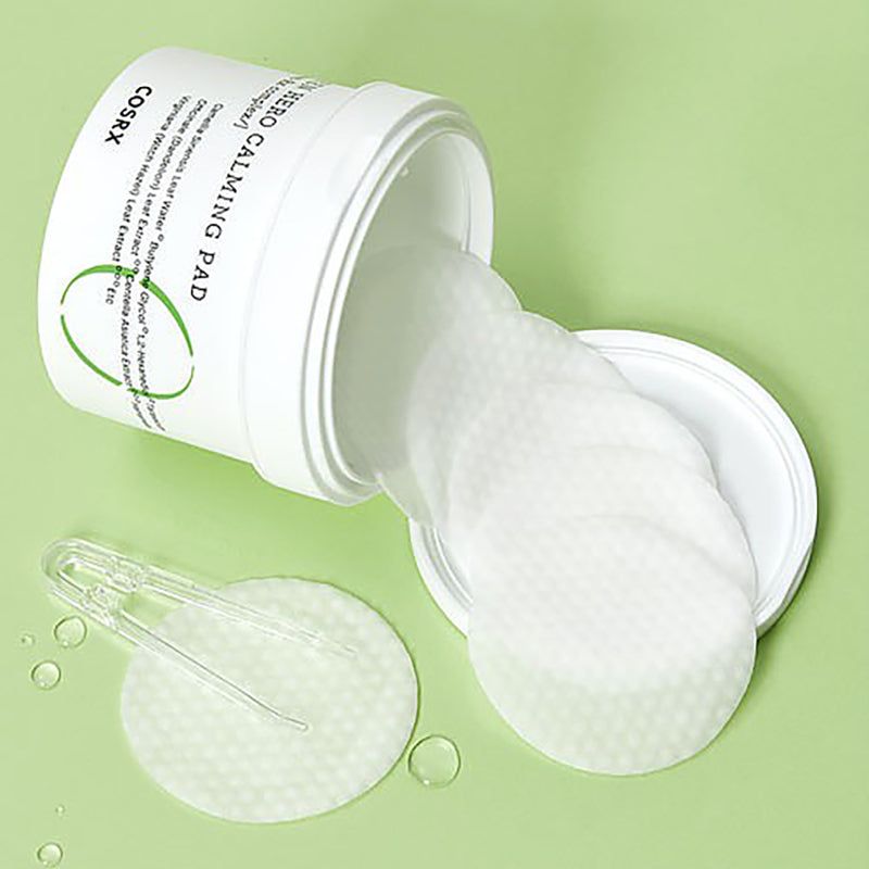 Witte pot met pads en pincet. Opschrift: Green Hero Calming Pad, COSRX. Groene achtergrond.