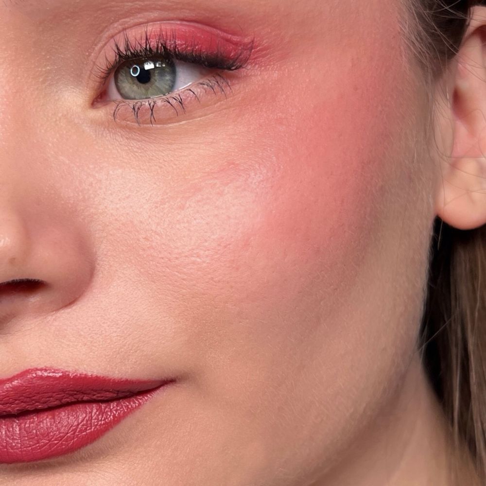 Gros plan d'un visage maquillé. Fard à paupières rouge, blush et rouge à lèvres. Œil vert.