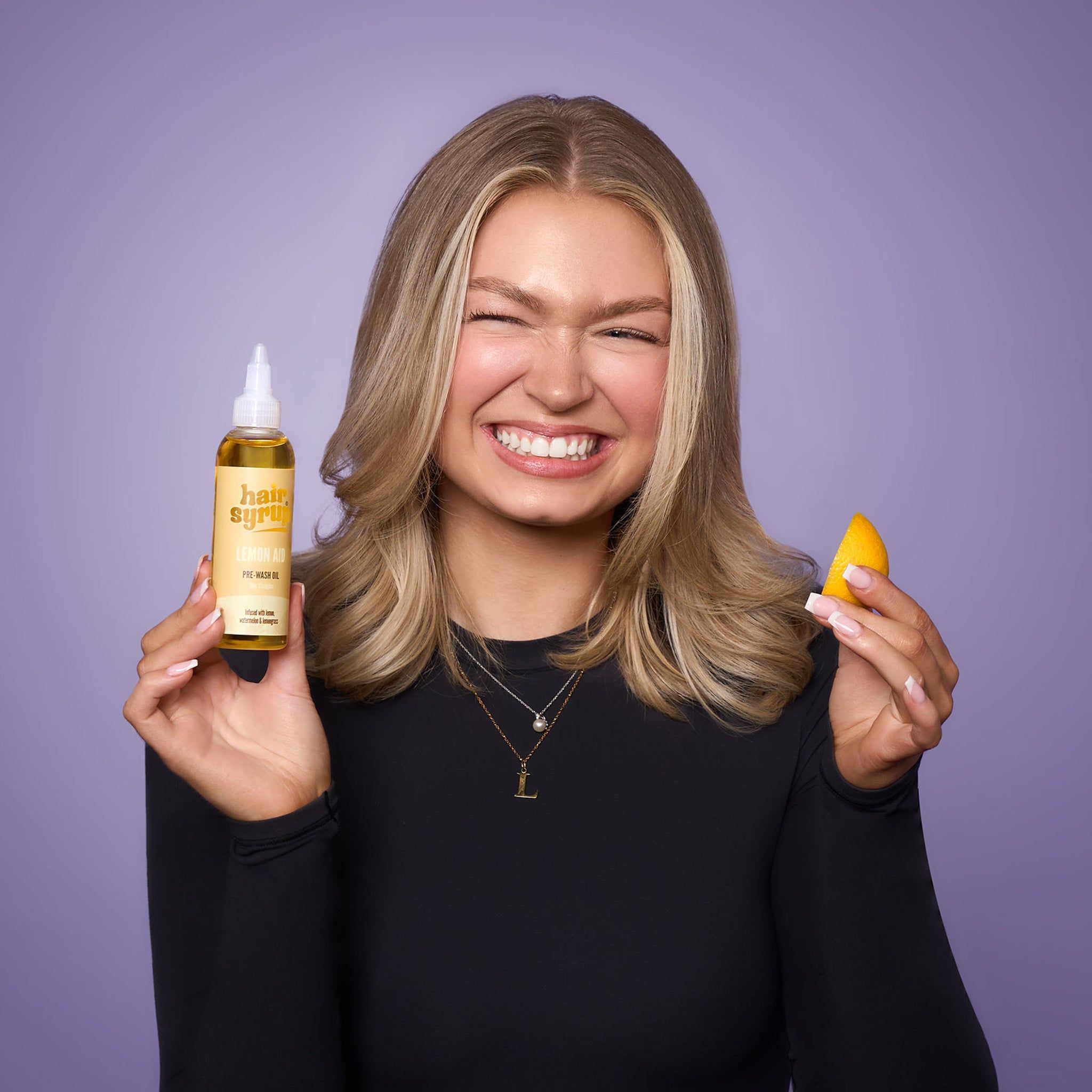 Vrouw met fles "Hair Syrup Vitamin C Me" en sinaasappelschijf. Pre-Wash Oil. Paarse achtergrond.