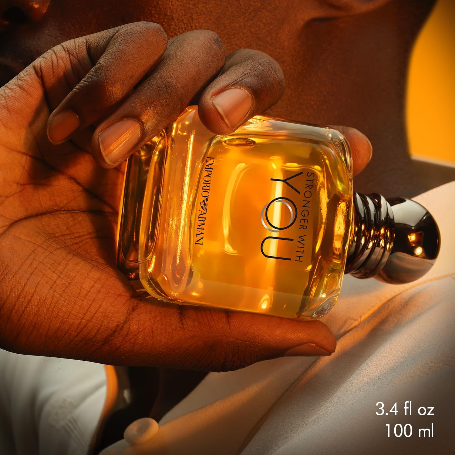 Fles in een hand. Opschrift: STRONGER WITH YOU en EMPORIO ARMANI. Tekst: 3.4 fl oz 100 ml.
