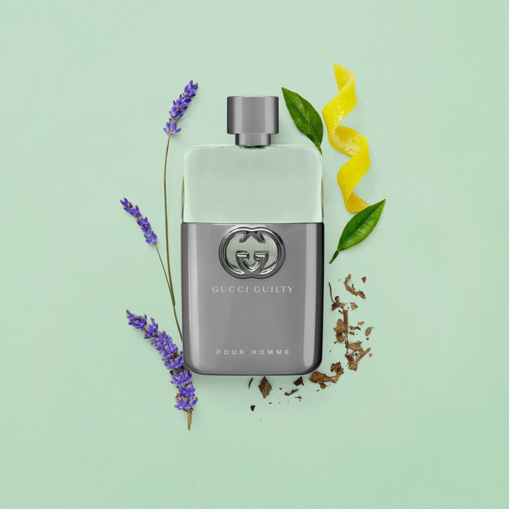 Flacon de Gucci Guilty Pour Homme. Flacon avec logo. Entouré de lavande, feuilles et zestes de citron sur fond vert.